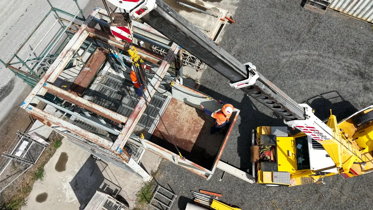 Top-down view of trainees guiding a steel frame into a bin under the crane hook